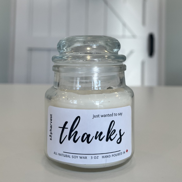 Glass jar candle with a 'thanks' label on a white surface