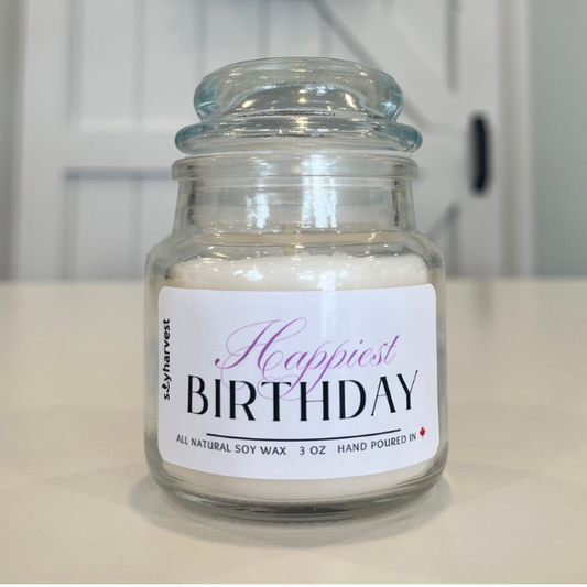 Glass jar candle labeled 'Happiest Birthday' on a white surface.