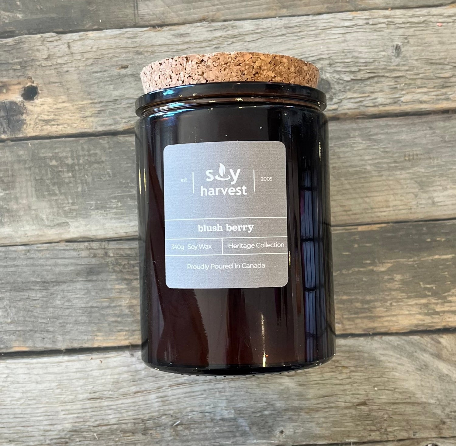 Black candle jar with cork lid on a wooden surface, featuring 'Soy Harvest' label.