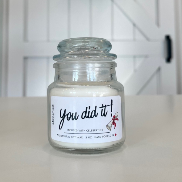 Candle in a glass jar with a 'You did it!' label on a white surface.
