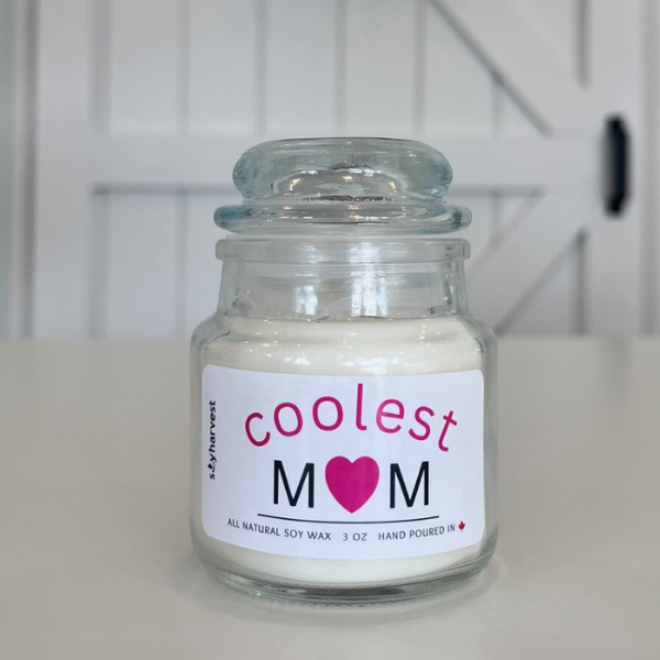 Candle jar labeled 'coolest mom' on a white surface with a blurred background