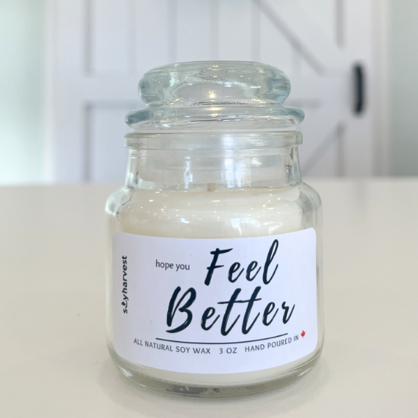 Glass jar candle with 'Feel Better' label on a white surface