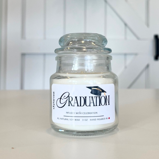 Glass jar candle labeled 'Graduation' on a white surface with a white background