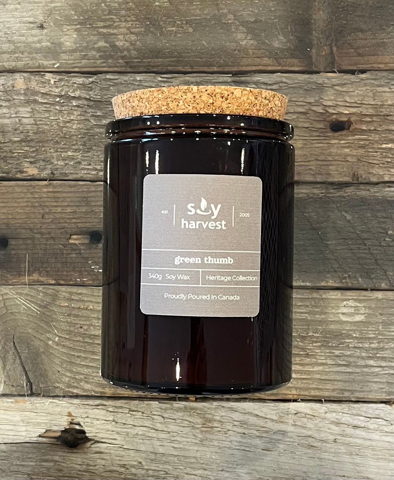 Black candle jar with cork lid on a wooden surface, featuring 'Soy Harvest' label.