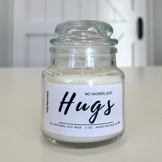 Candle jar with a label reading 'No words, just hugs' on a white surface.