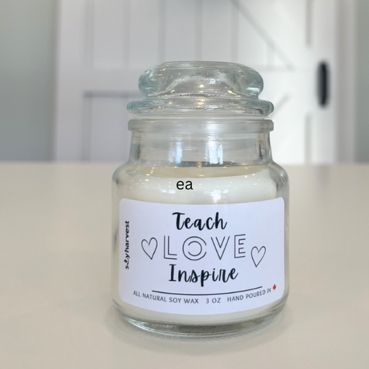 Glass jar candle with a label reading 'Teach Love Inspire' on a white surface.